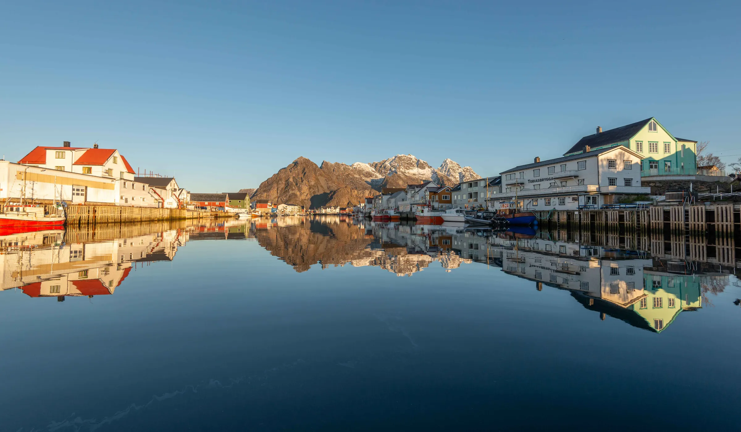 Desa nelayan Henningsvaer di Lofoten, Norwegia, rumah kayu di tepi air dengan pegunungan bersalju di kejauhan