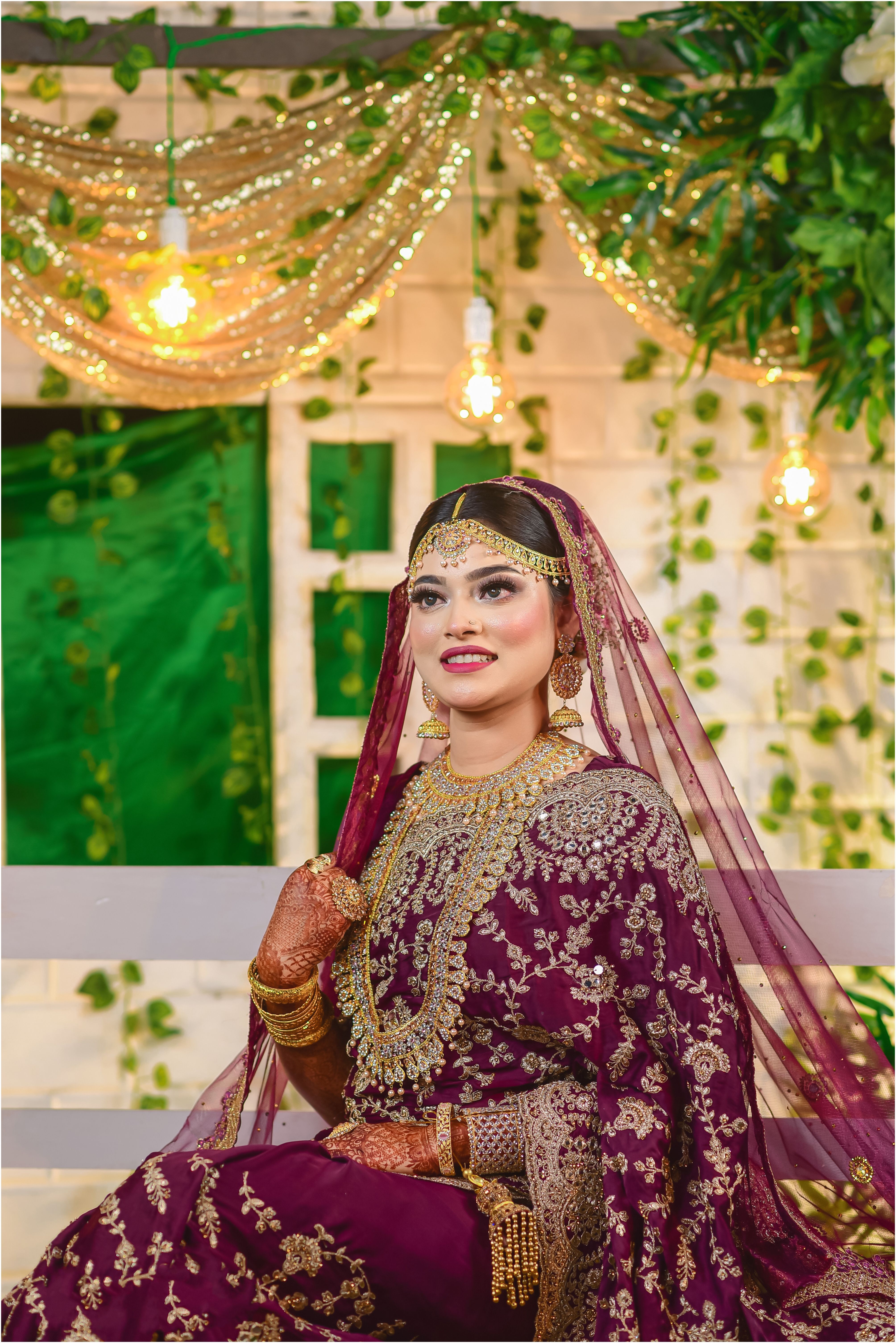 A young South Asian bride in ornate traditional clothing, posing indoors.