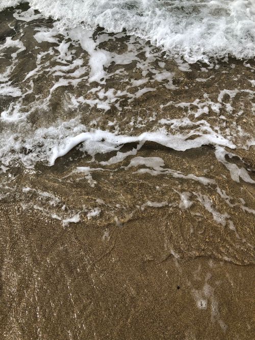 Free Close-up of ocean waves crashing onto a sandy beach, creating foam and texture. Stock Photo