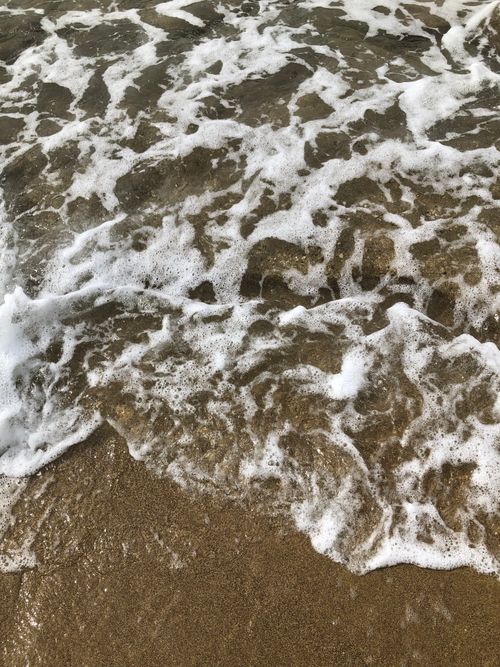 Free Foamy ocean waves gently wash over a sandy beach, capturing the beauty of the sea. Stock Photo