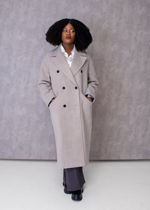 Photo of a Woman with Afro Hairstyle Wearing a Gray Coat, Posing against a Gray Wall