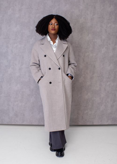 Free Stylish woman with afro hairstyle wearing a long gray coat, posing elegantly indoors. Stock Photo