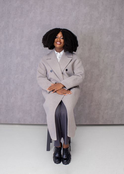 Free Stylish woman wearing a gray coat sitting and posing in a studio setting. Stock Photo