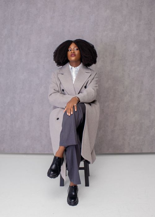 Free Stylish portrait of a woman in a grey coat sitting poised in a studio setting. Stock Photo