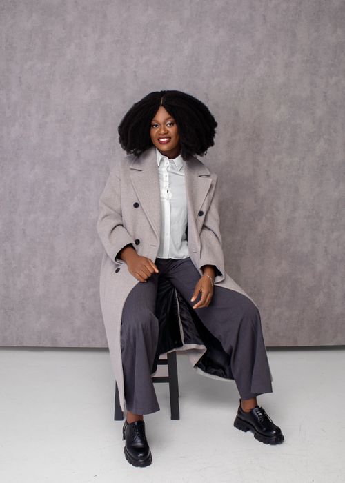 Free Portrait of a stylish woman in a chic outfit sitting against a gray backdrop, exuding elegance and confidence. Stock Photo