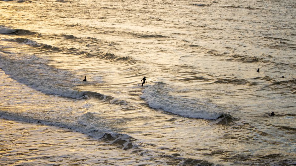 Surfers enjoying the ocean waves during sunset, captured from above.