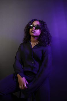 Black woman posing with confidence in a stylish studio portrait, wearing sunglasses and classic attire.