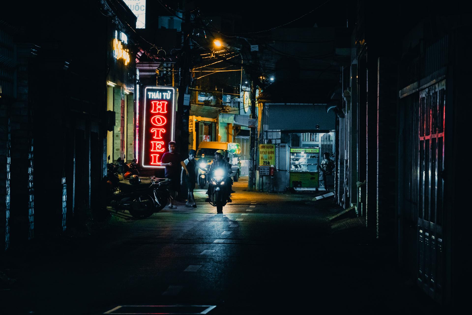 A vibrant city street scene at night with neon hotel signs and motorcycles creating an urban atmosphere.