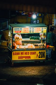 Illuminated street food kiosk selling Banh Mi at night in a bustling city street.