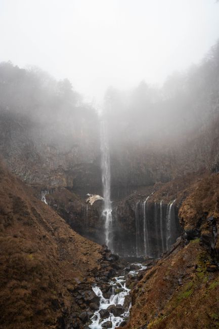 A breathtaking view of a waterfall cascading down a foggy mountain in autumn.