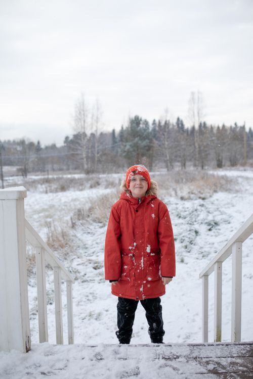 Free Child in red jacket and beanie standing on snowy porch steps, embracing a winter day. Stock Photo
