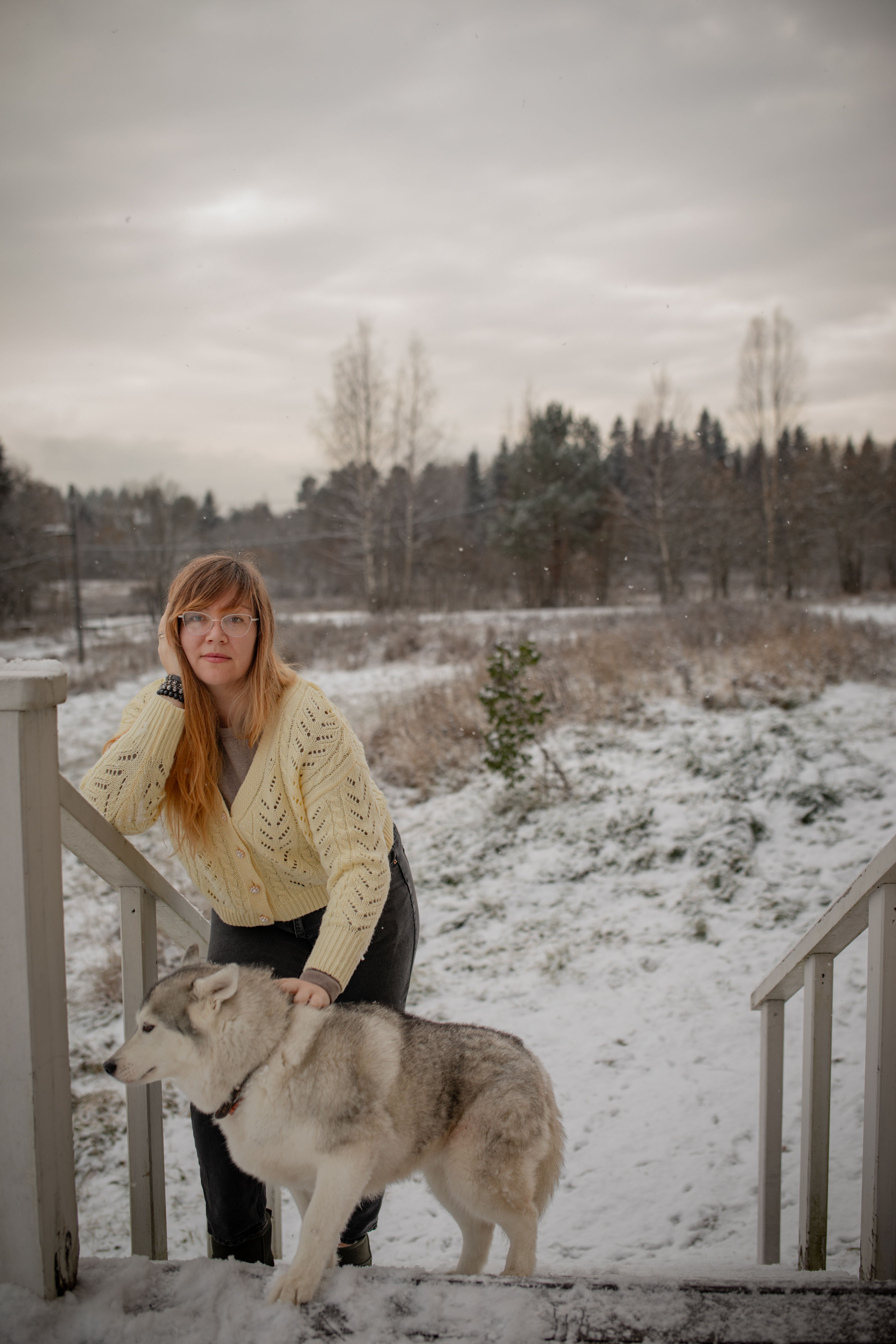 A woman in a wintery outdoors poses with a husky dog, creating a serene scene.