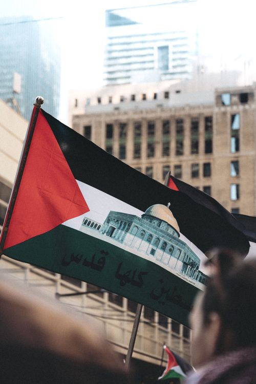 Free A Palestinian flag waved at a city protest. Urban background emphasizes the protest theme. Stock Photo