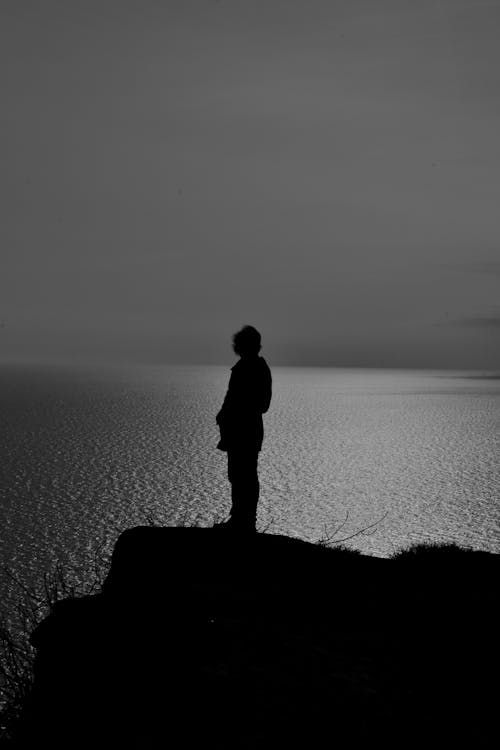 Person Standing at Edge of Rock by Ocean