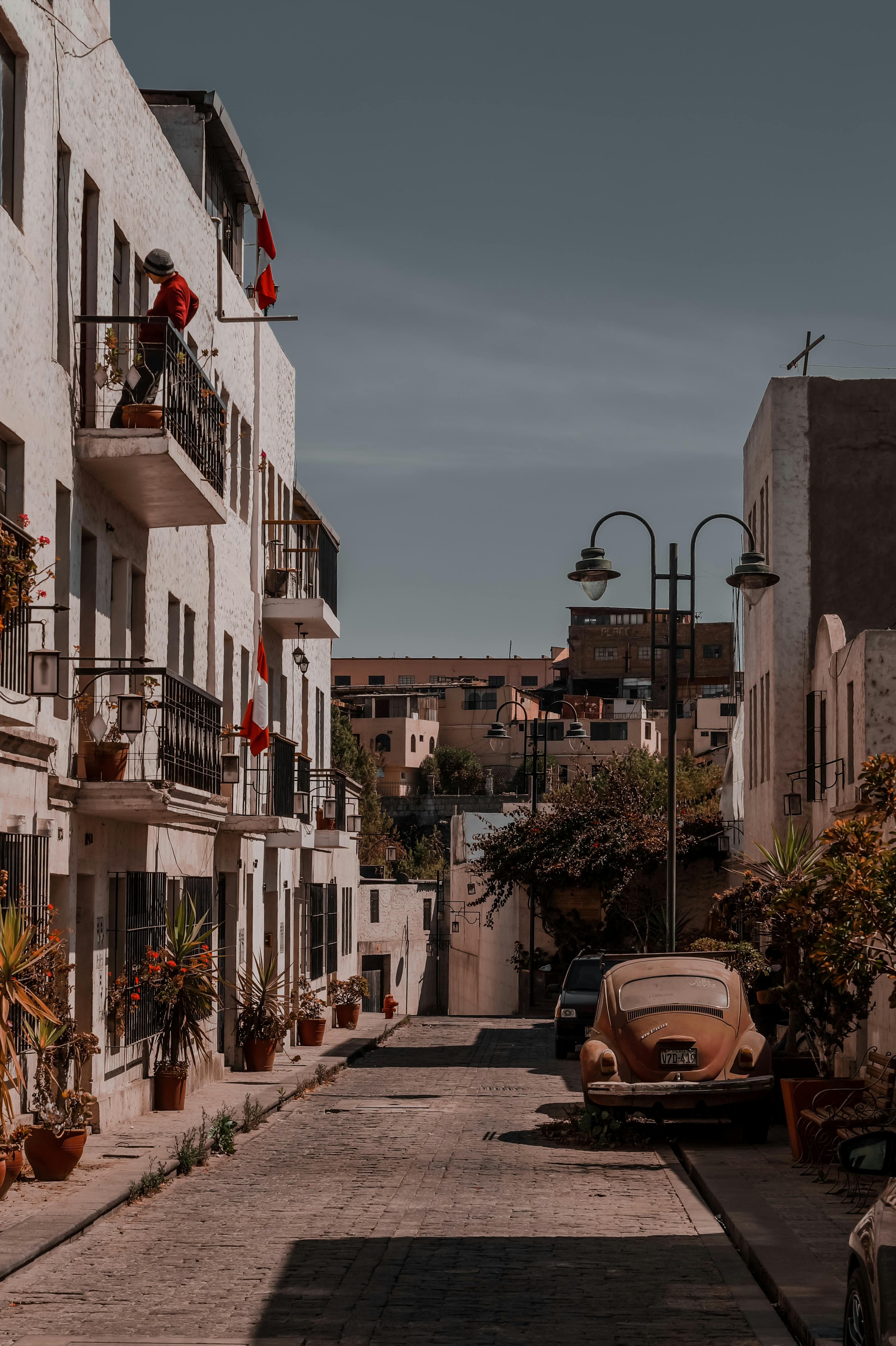 Quiet street in Arequipa, Peru with townhouses and vintage car, showcasing urban life.