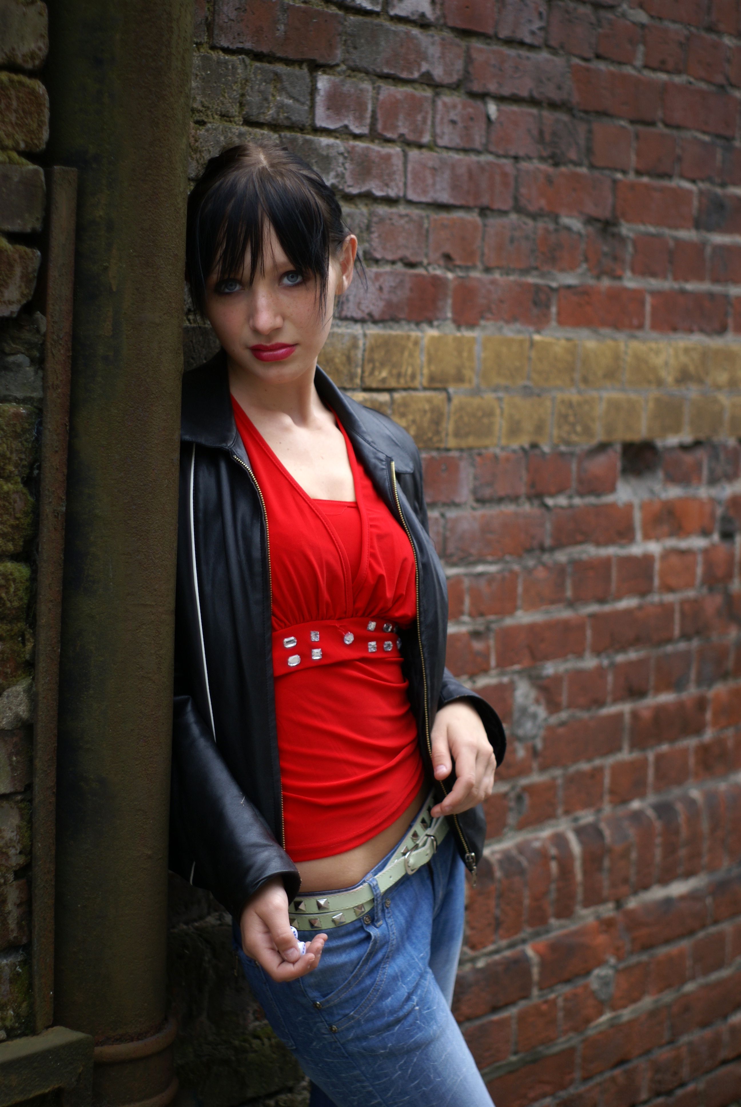 A woman leaning against a brick wall wearing a red shirt and jeans ...
