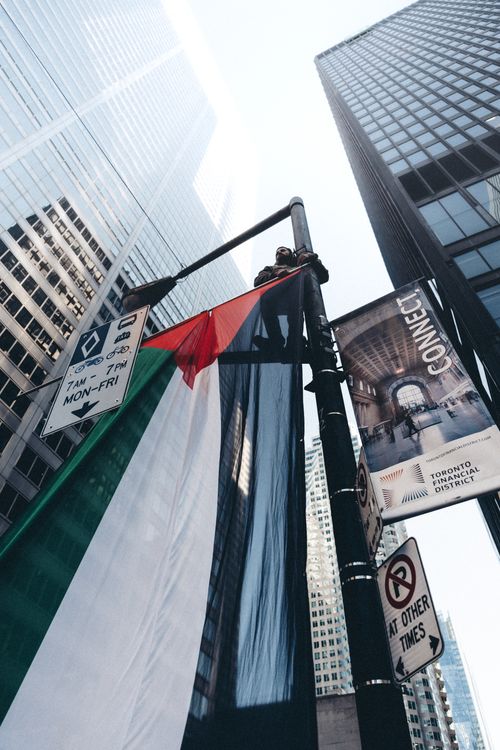 Free Palestinian flag draped over a street lamp amidst towering skyscrapers in an urban setting. Stock Photo