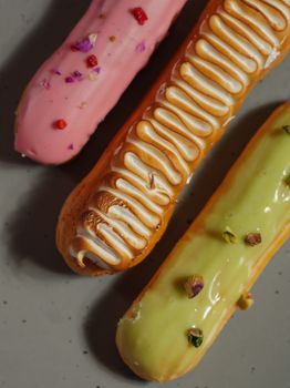 Close-up of three colorful eclairs with unique toppings on a gray surface.