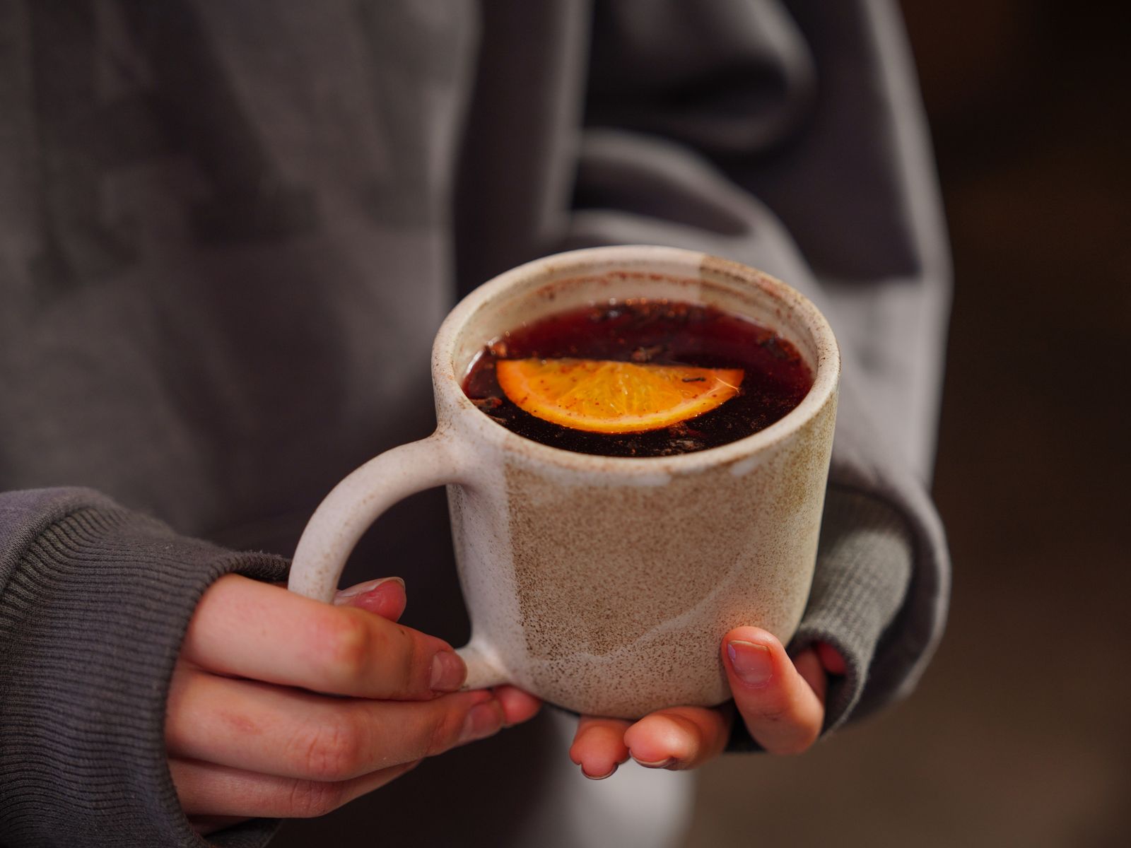 Warm close-up of a person holding a tea mug with a slice of lemon. Perfect for cozy autumn vibes.