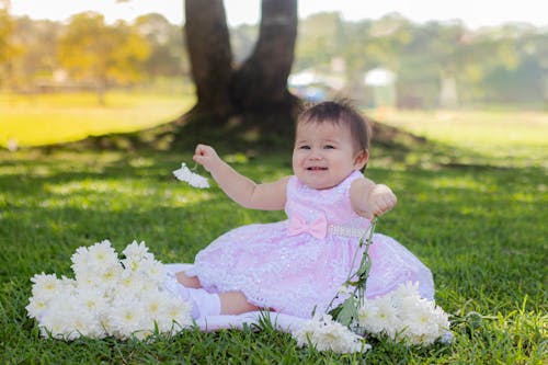 Happy Little Girl in Pink Dress Sitting on Grass