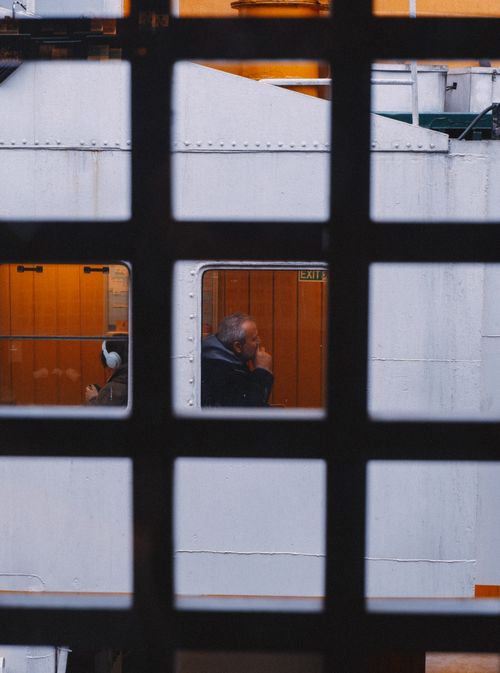 Free Shot of a man sitting inside a train compartment viewed through a window grid. Stock Photo