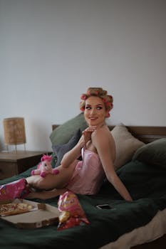 Woman with rollers in hair sitting on bed enjoying a relaxed moment indoors.