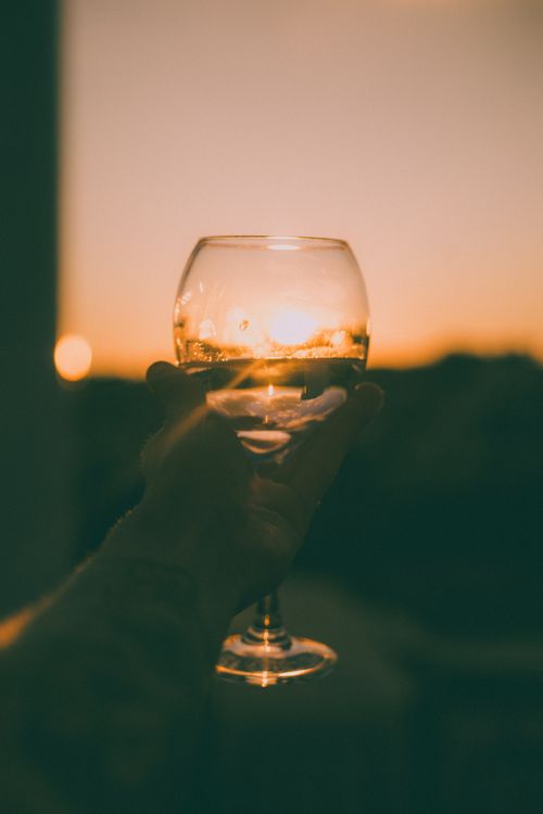 Free A hand holding a wine glass against the backdrop of a warm sunset, symbolizing celebration. Stock Photo