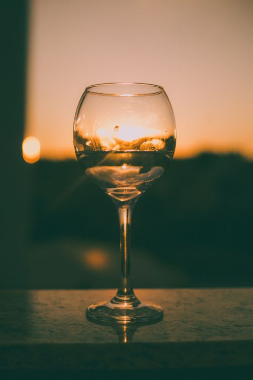 Free A wineglass beautifully reflecting sunset hues on a windowsill, creating a serene and elegant ambiance. Stock Photo