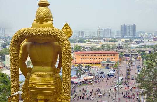 Aerial view of Batu Caves with the golden Murugan statue and Kuala Lumpur cityscape beyond.