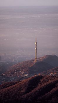 Distant view of the Almaty Tower atop foggy hills during dawn, showcasing a serene landscape.