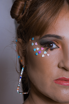 Close-up of a woman with artistic makeup and colorful heart embellishments, exuding a glamorous vibe.