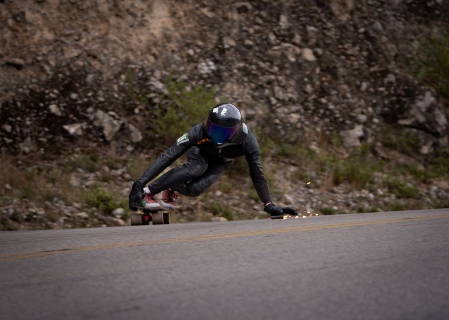 A skateboarder in full gear speeds downhill on a road, showcasing daring skill and control.