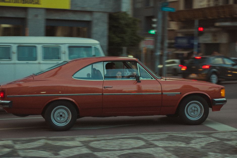 Fotomural Coche clásico rojo circulando por las calles de la ciudad, capturando la vibra urbana y la estética vintage.