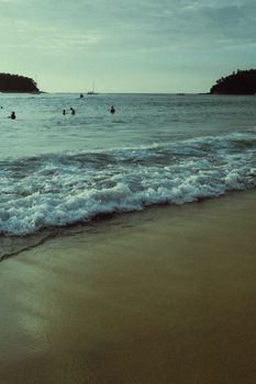 Capture of tranquil waves on a sandy beach at sunset, featuring distant swimmers.