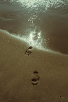 Sunlit footprints on Karon Beach's wet sand in Phuket, Thailand, next to gentle waves.