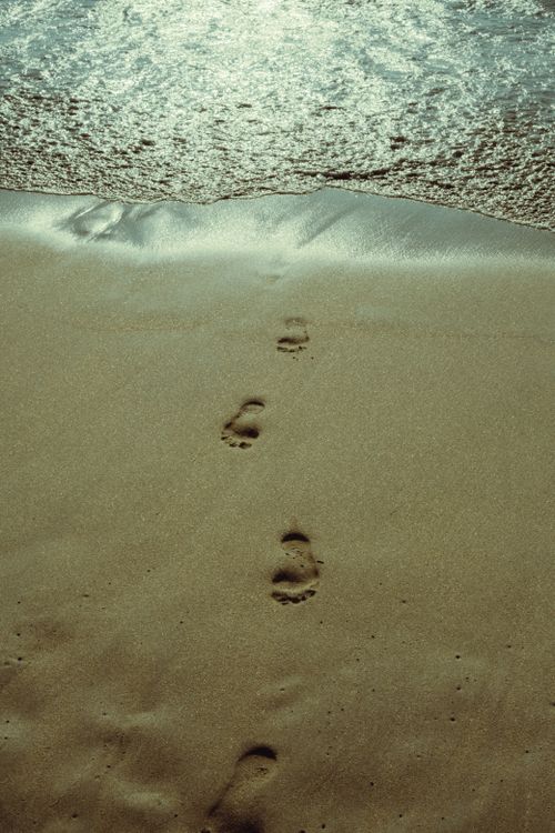 Free Footprints leading to the sea on a sunny beach, perfect for travel and relaxation themes. Stock Photo