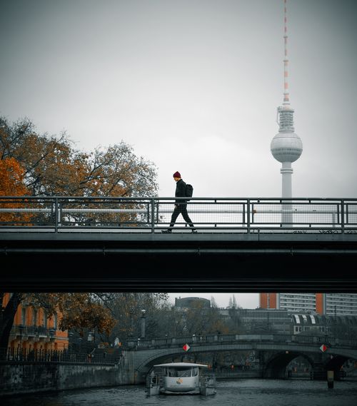 Free A man walks on a bridge in Berlin with the famous Fernsehturm in the background. Stock Photo