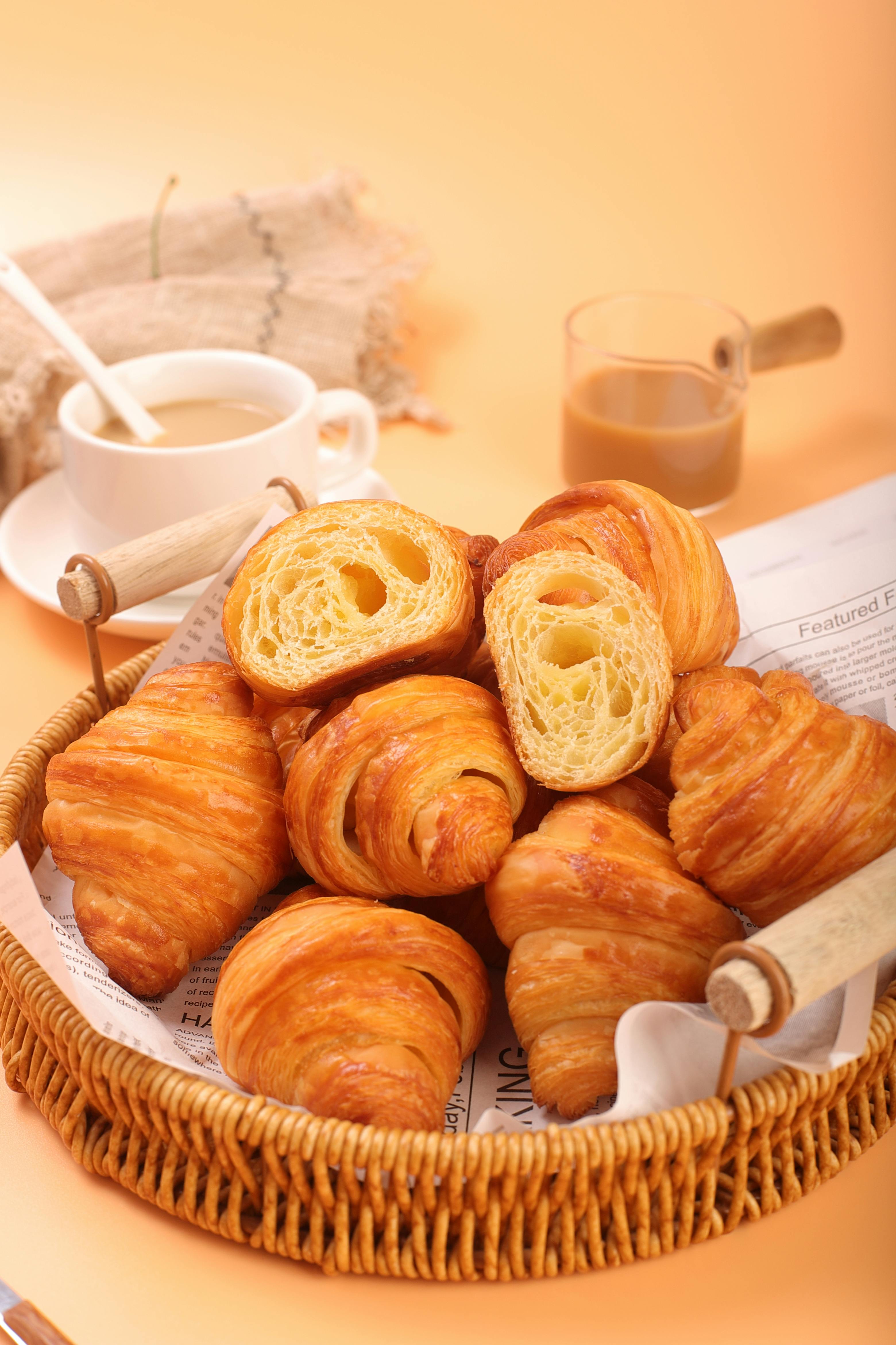 Warm and flaky croissants displayed in a wicker basket with a coffee cup in the background.