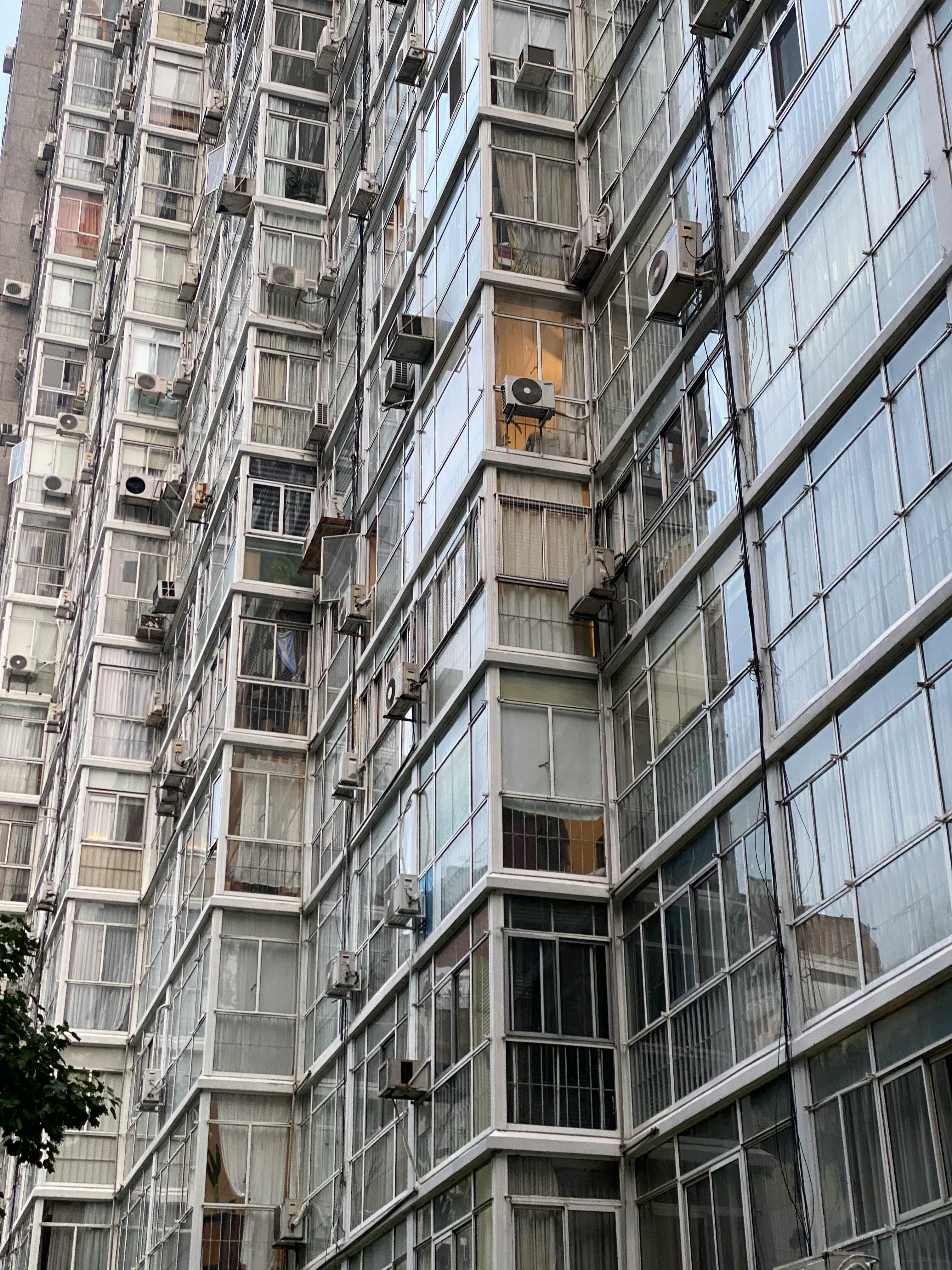 Tall apartment building with grid-like pattern of windows and air conditioning units.