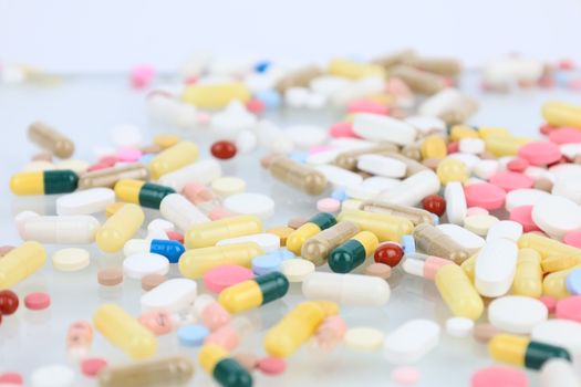 A vibrant assortment of pills and capsules scattered across a white surface representing medication and healthcare.