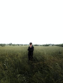 A man in a suit stands in a grassy field under an overcast sky in Grasse, France.