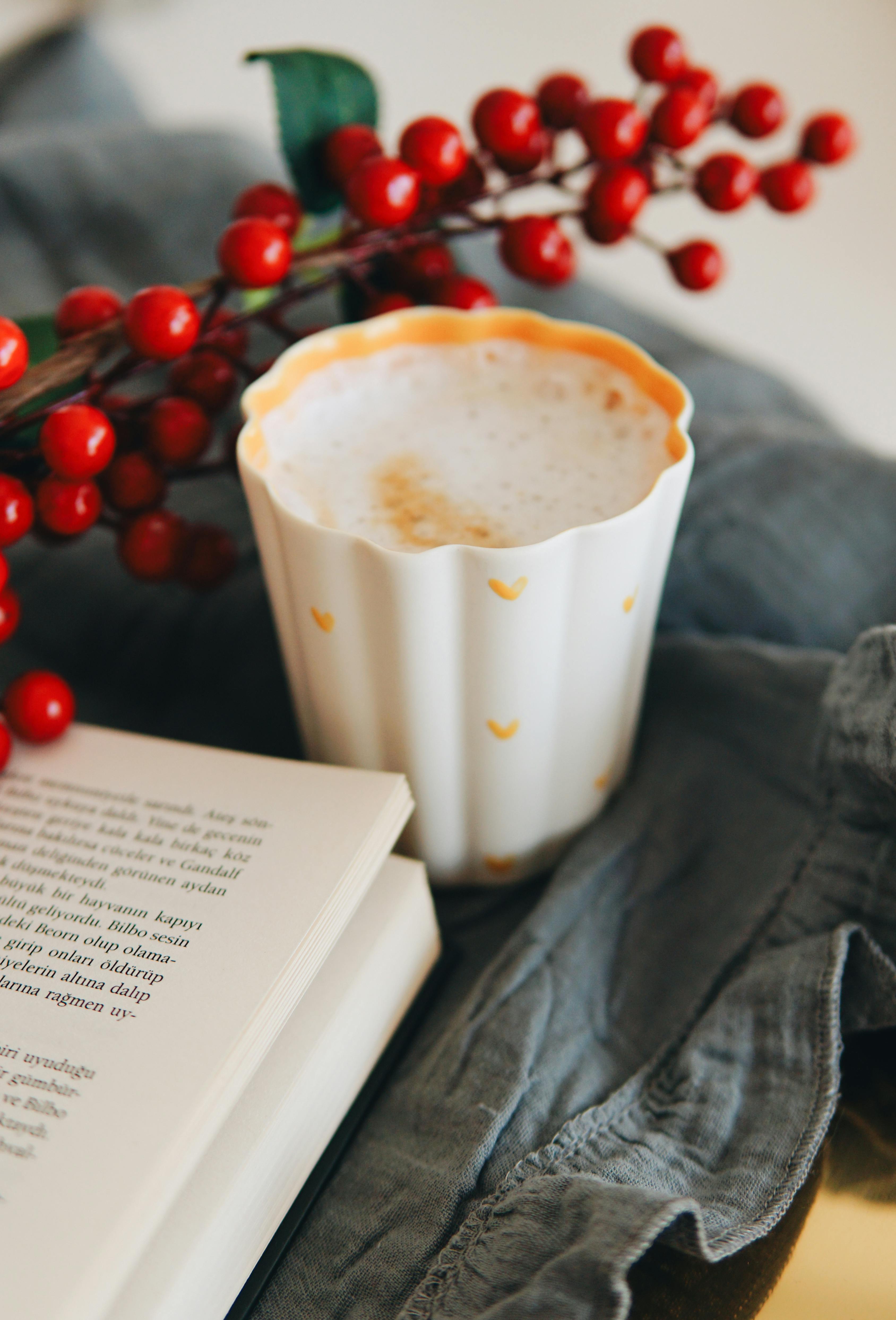 A warm cappuccino with a book and rowanberries creating a cozy atmosphere.