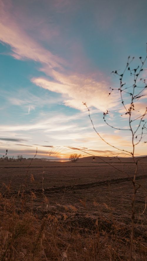 Free Beautiful sunset over a vast farmland with dramatic sky and clouds, creating a peaceful scene. Stock Photo