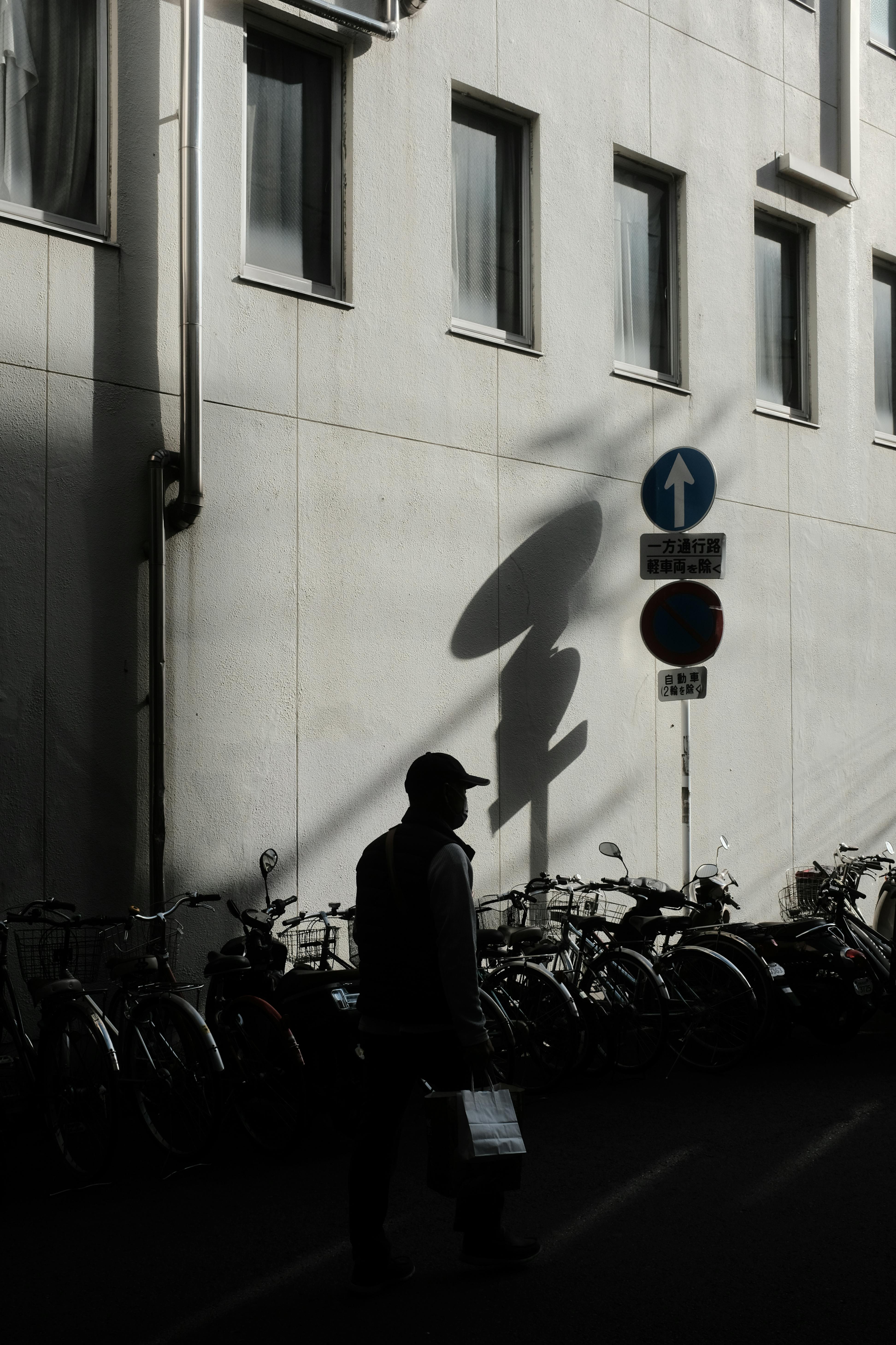 Urban scene with a shadowed man walking past bicycles and building signs.