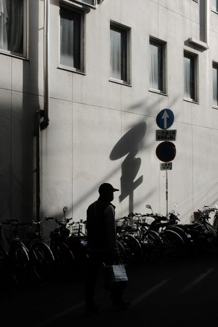 Urban scene with a shadowed man walking past bicycles and building signs.