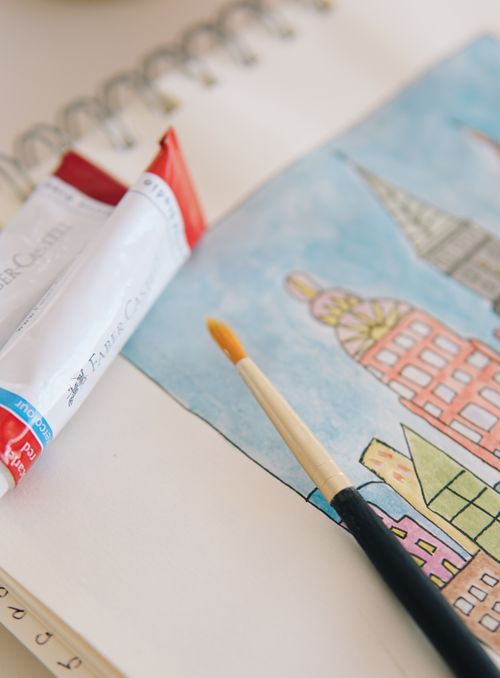 Free Notebook open to a watercolor painting of cityscape with paintbrush and tube in view. Stock Photo