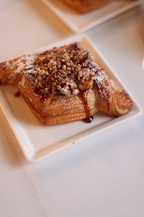 Free Close-up of a croissant dessert topped with walnuts and maple syrup on a white plate. Stock Photo