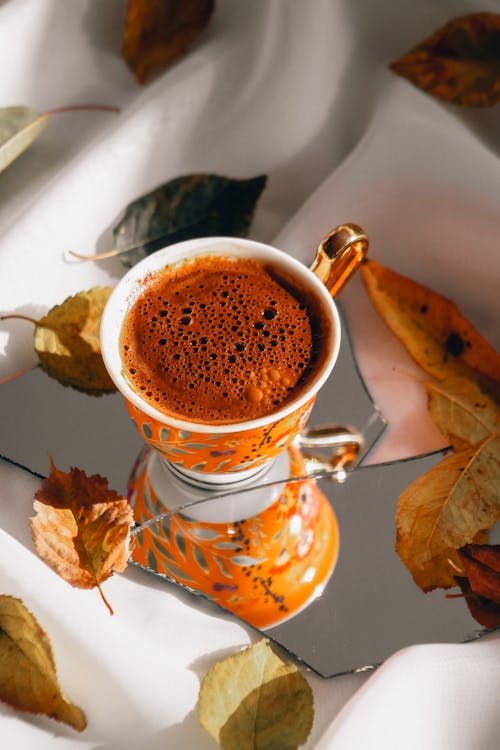 Coffee Cup on Pieces of Broken Mirror Among Autumn Leaves