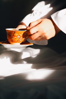 Close-up of hands holding an ornate tea cup and saucer with soft lighting.