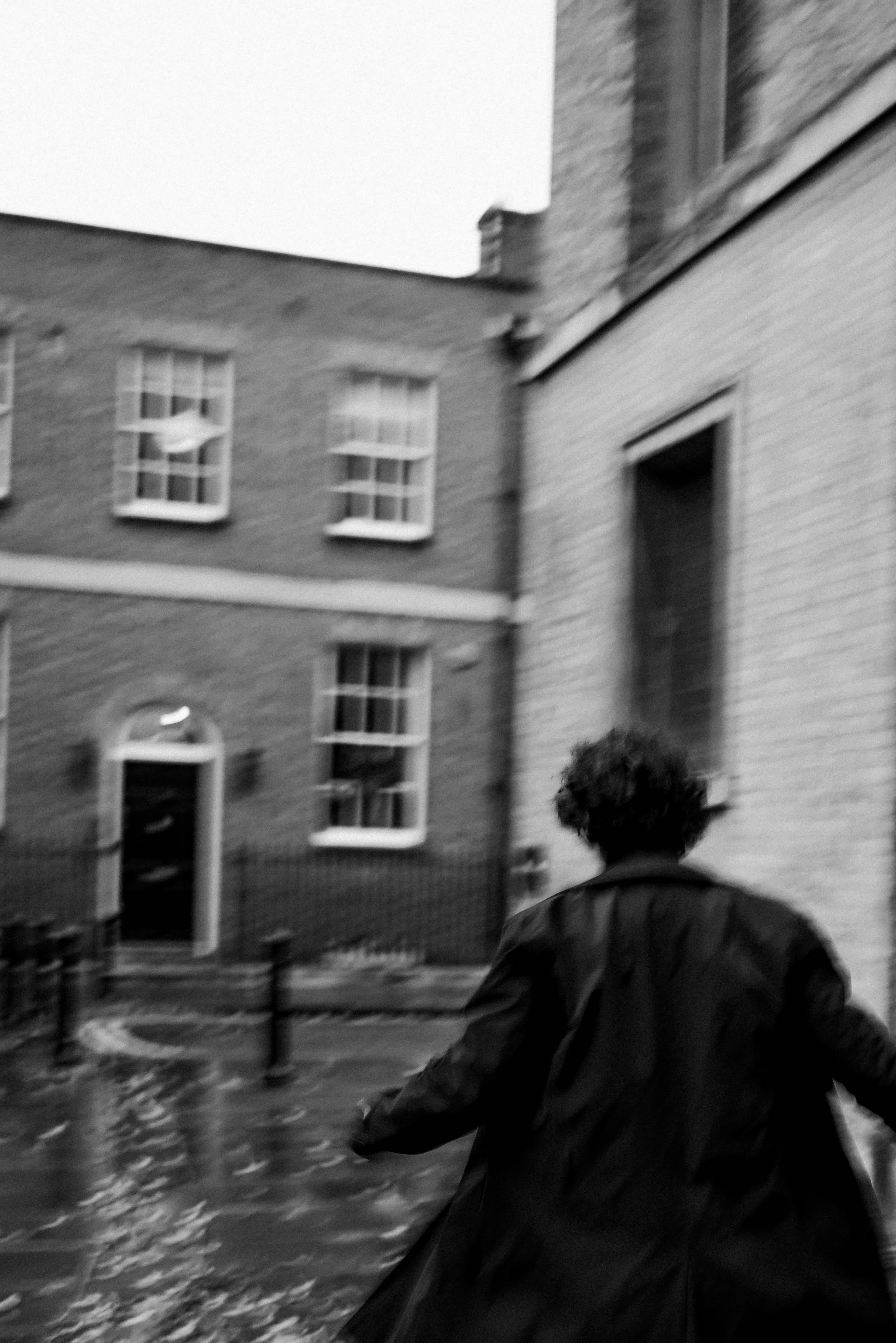 Blurred black and white photo of a man running down a wet city street in fall.